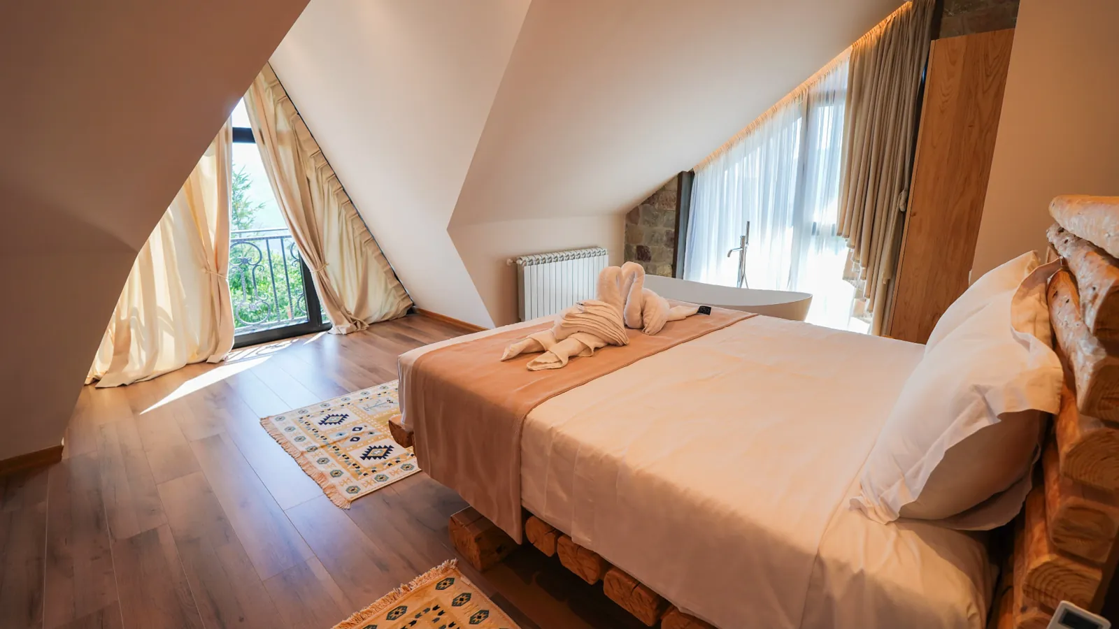 Top-floor suite with timber bed, balcony door and a freestanding bathtub