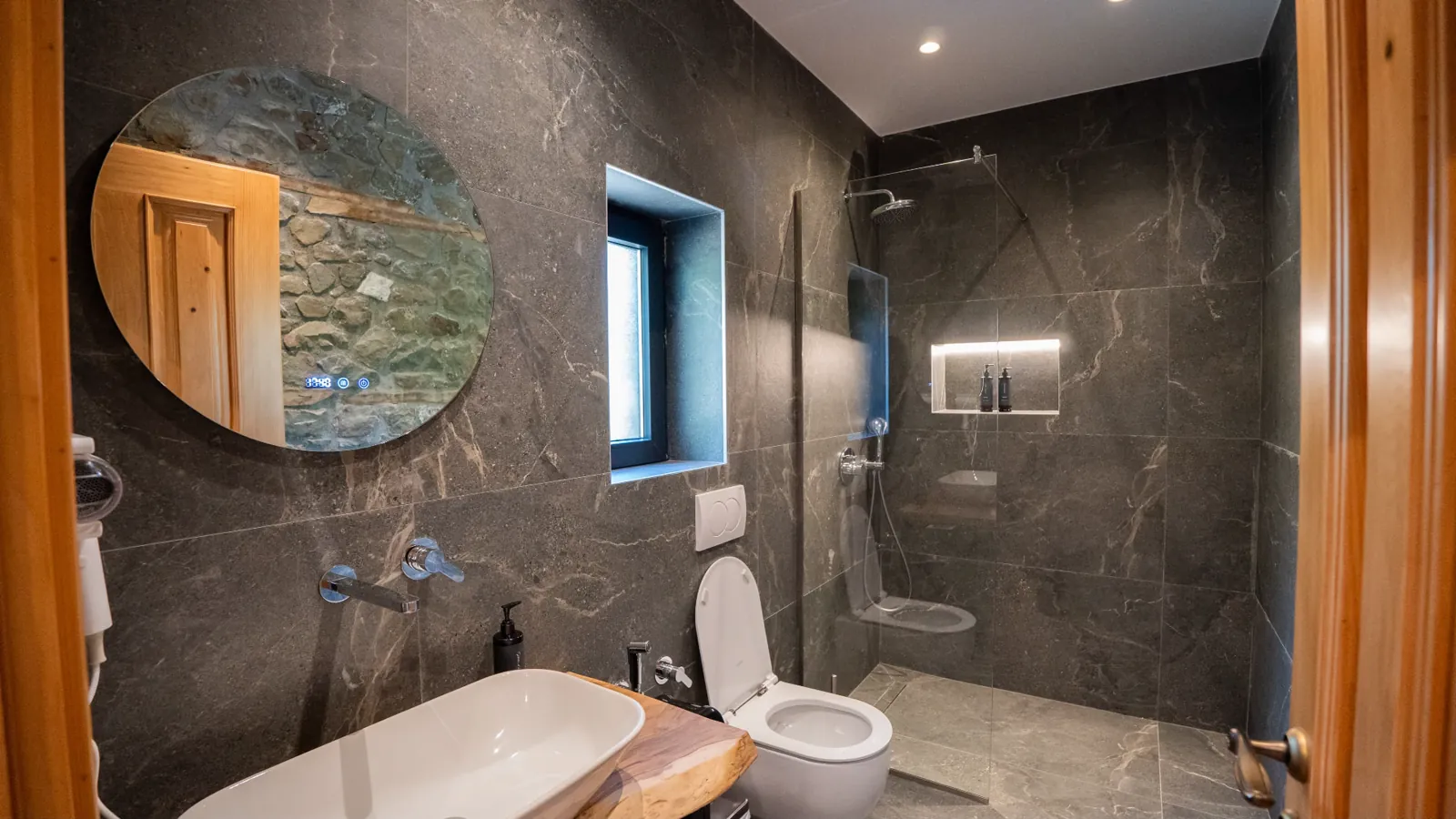 Bathroom with a glass shower, wooden vanity and round mirror
