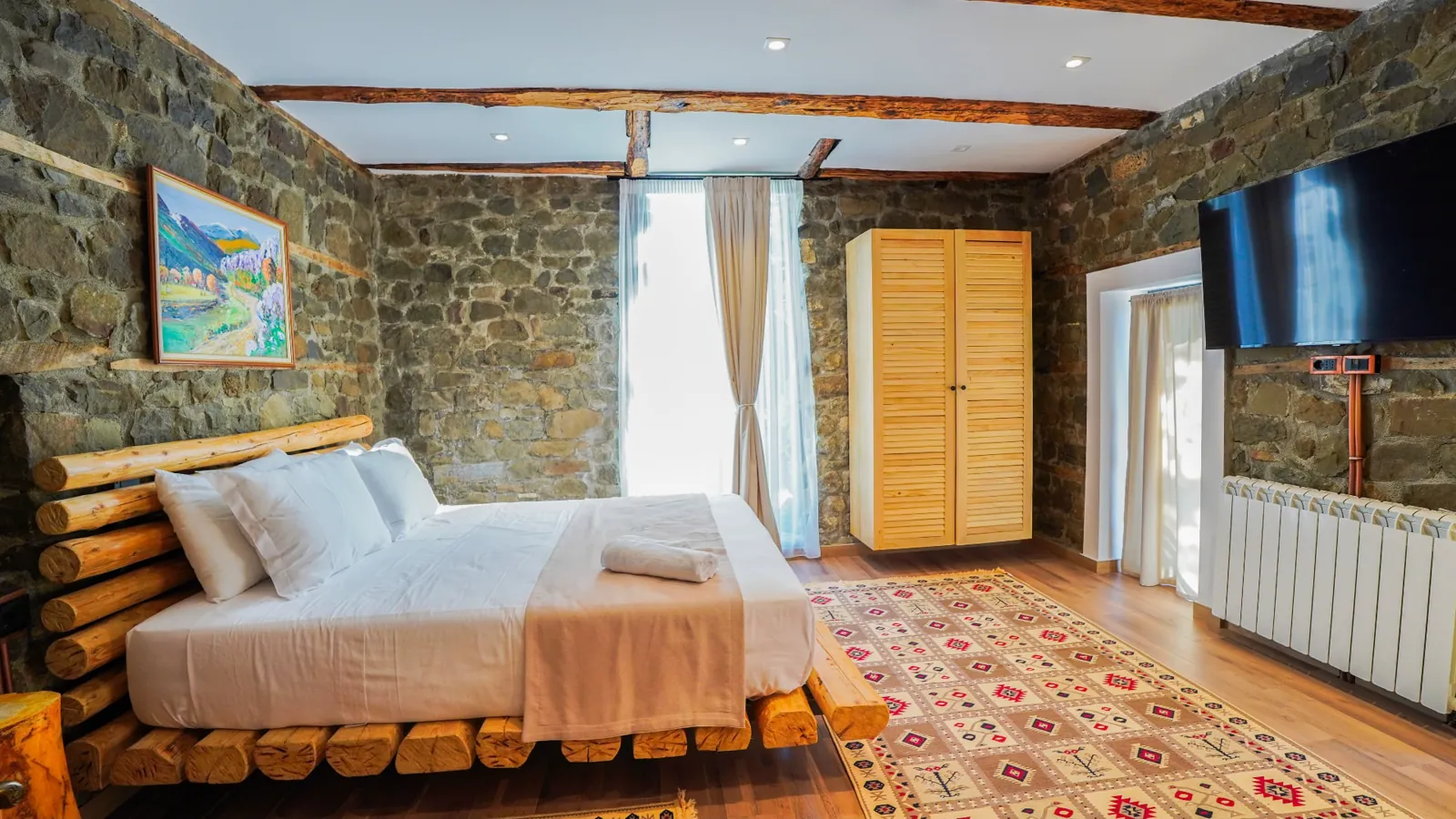 Bedroom with exposed stone walls, log bed and traditional rugs