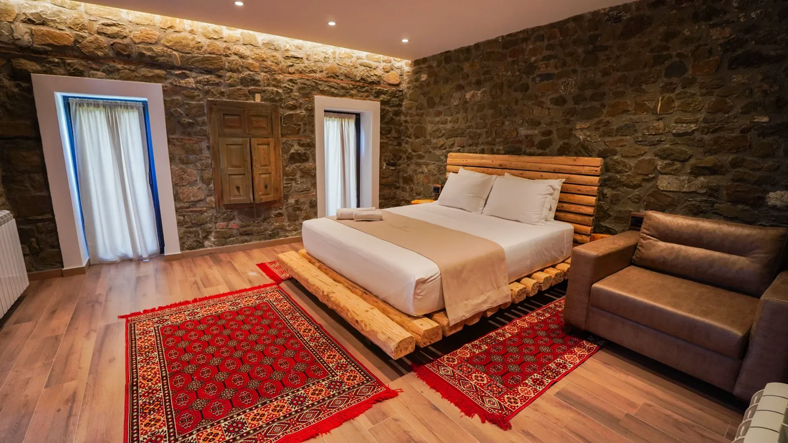 Stone-walled bedroom with a wooden bed and patterned rugs